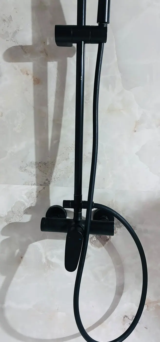 Grifo de ducha negro mate y barra sobre azulejo claro.