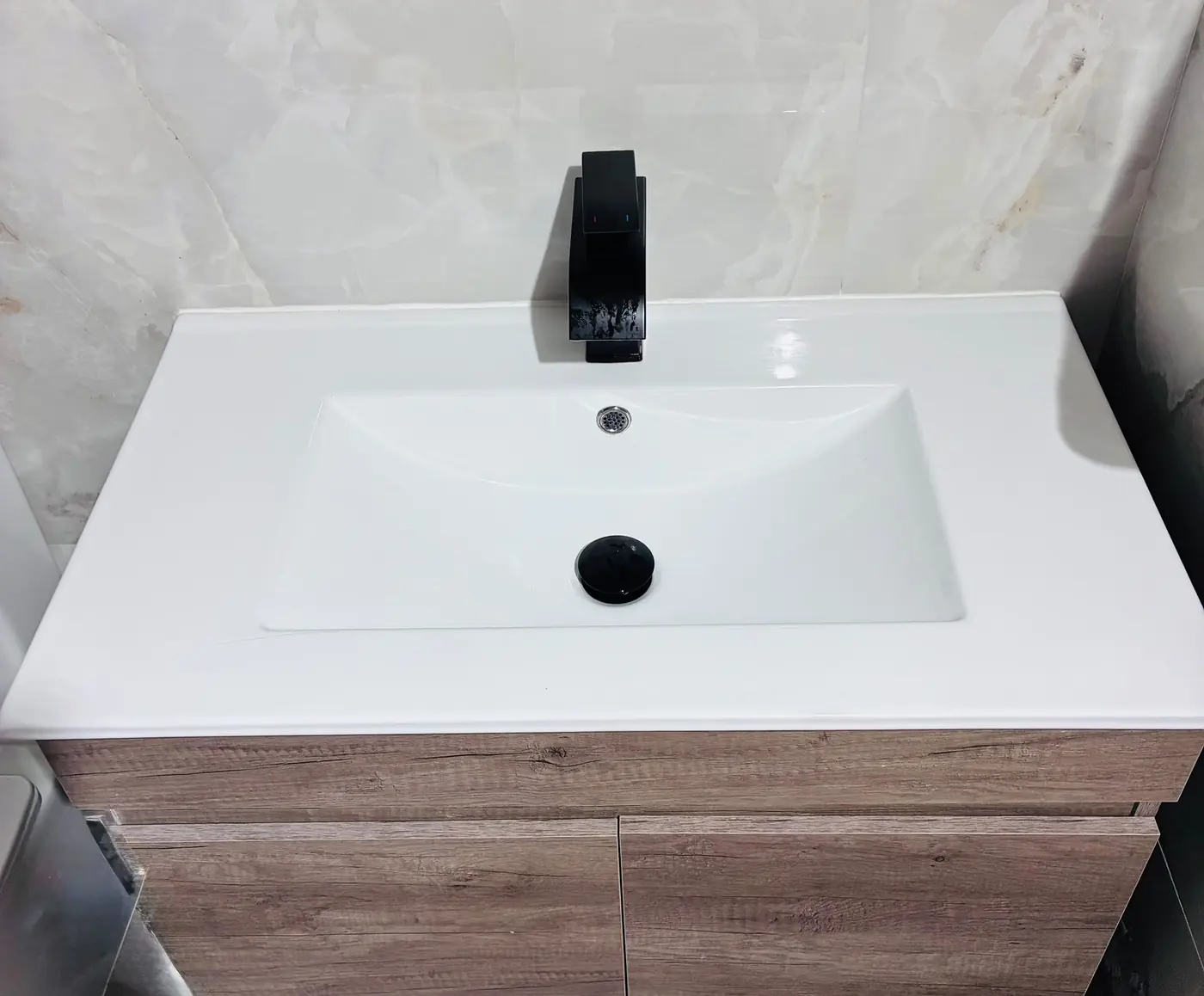 Lavabo blanco con grifo negro mate sobre mueble de madera.
