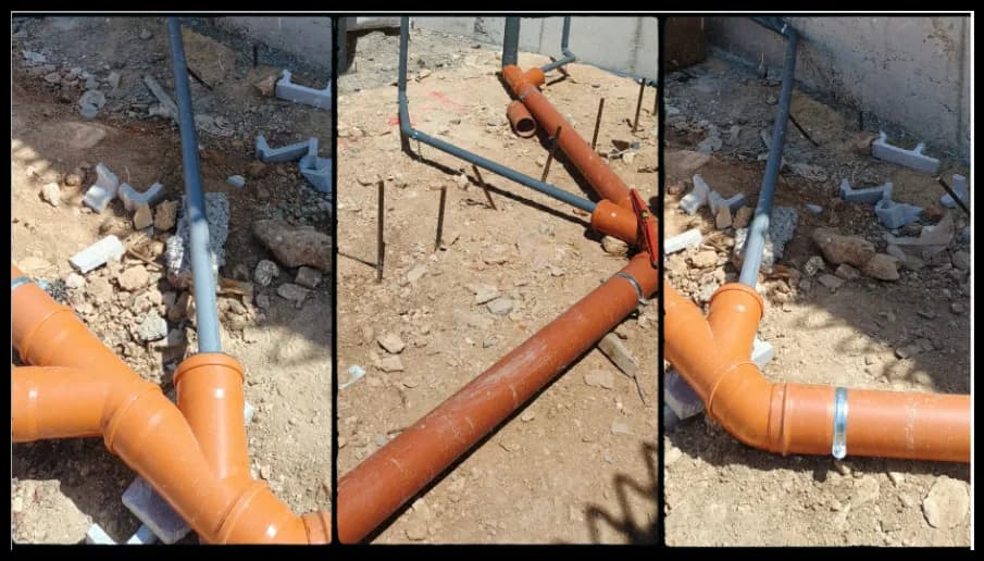Colectores de saneamiento naranjas y bajante en zanja de obra.